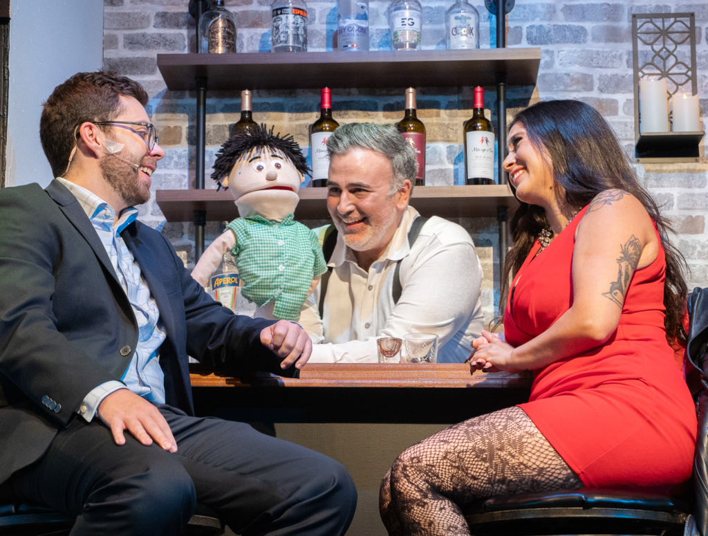 two people sitting at a bar while the bar tender entertains them with a puppet